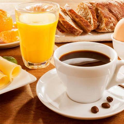 Breakfast table with coffee, pastries, muesli, eggs, fruit and juice in detail