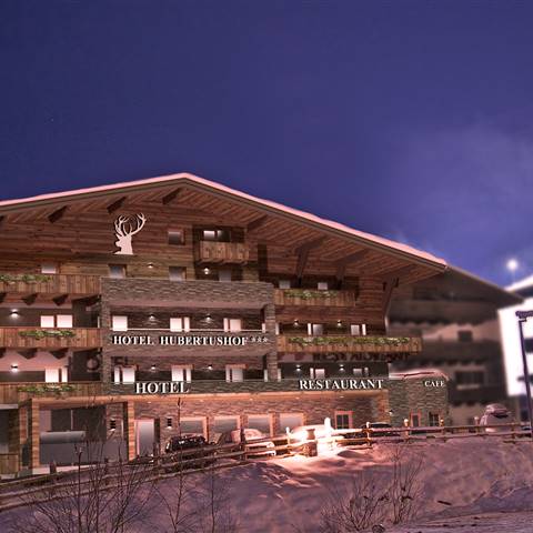 An alpine hotel illuminated at night with a snowy mountain in the background